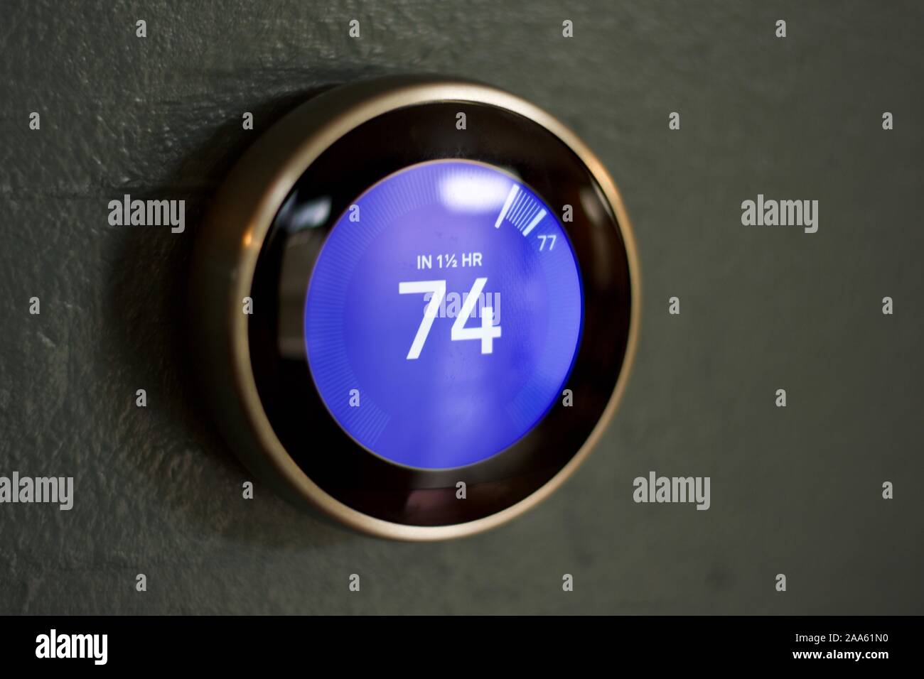 Smart Thermostat durch männliche Hand gegen eine blaue Wand angepasst werden. Smart Thermostat auf dunklen blauen Wand. Kleine Reflexion vorhanden Stockfoto