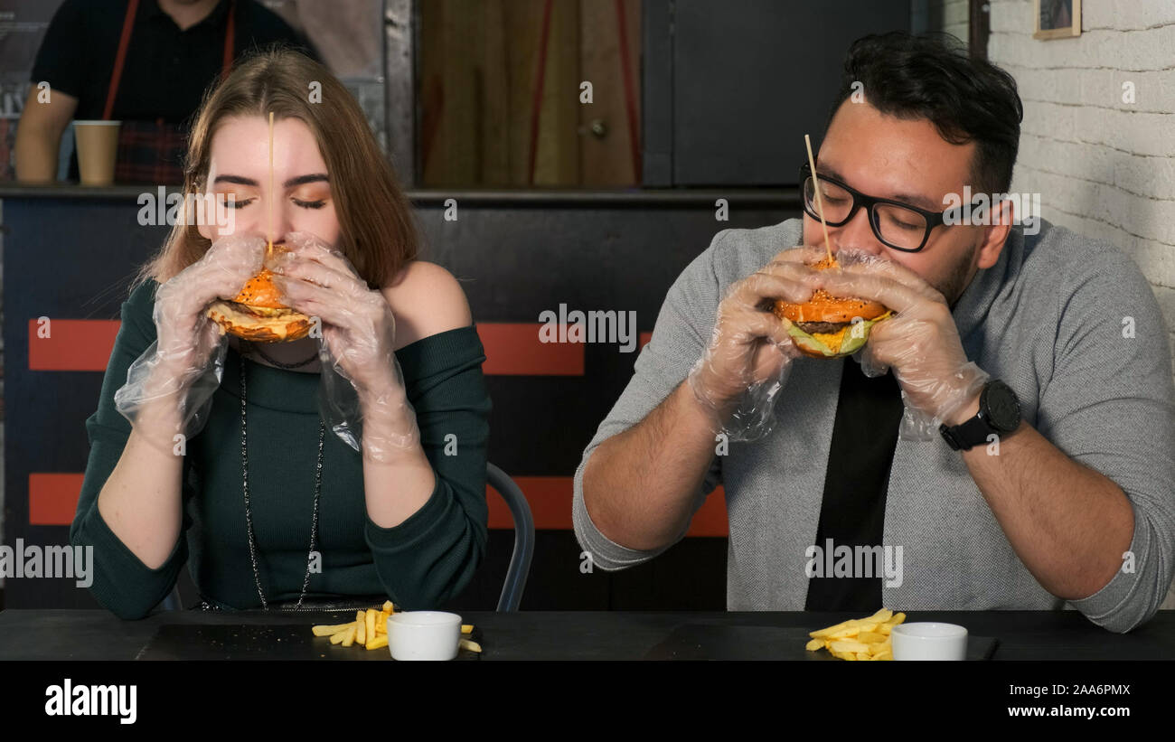 Gemischtrassiges Paar essen Burger in einem Café. Asian guy Bites einen leckeren Burger Stockfoto