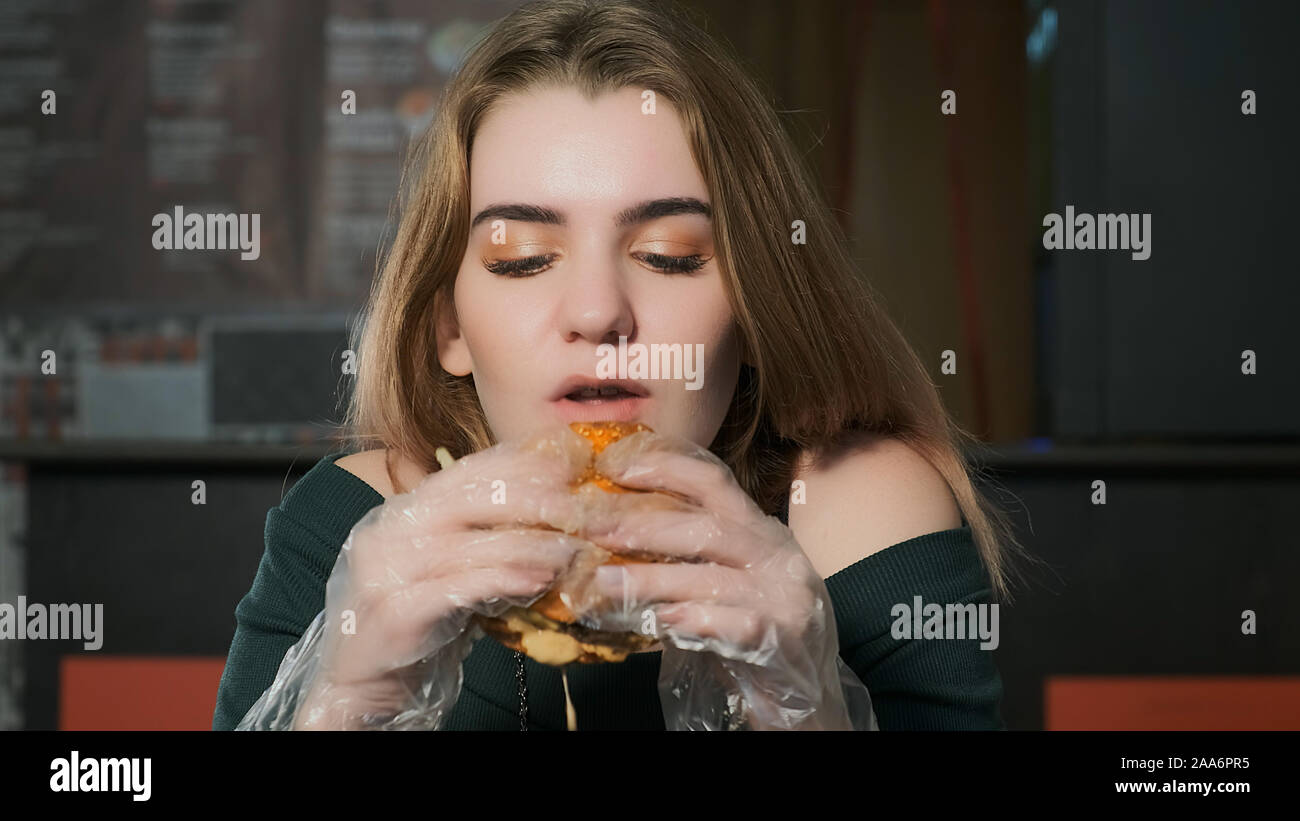 Junge schöne Frau isst einen Hamburger in einem Café. Lecker junk food Stockfoto