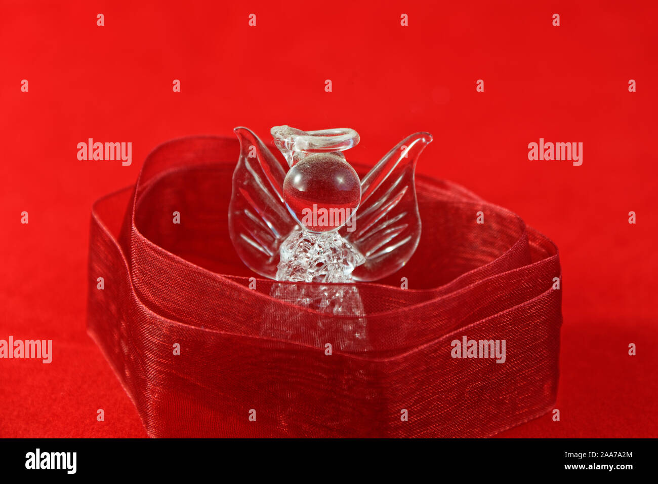 Ein Glas Engel ist in Red Ribbon auf rotem Hintergrund gewickelt Stockfoto
