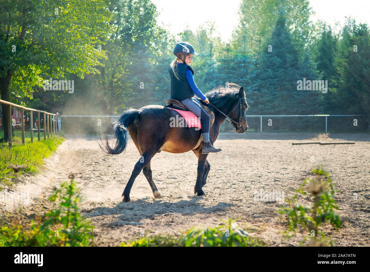 Ein junges Mädchen reiten ihr Pony während der Reitstunde, außerhalb. Natürliche Sonnenstrahlen im Staub während des Sonnenuntergangs zu glänzen. Stockfoto