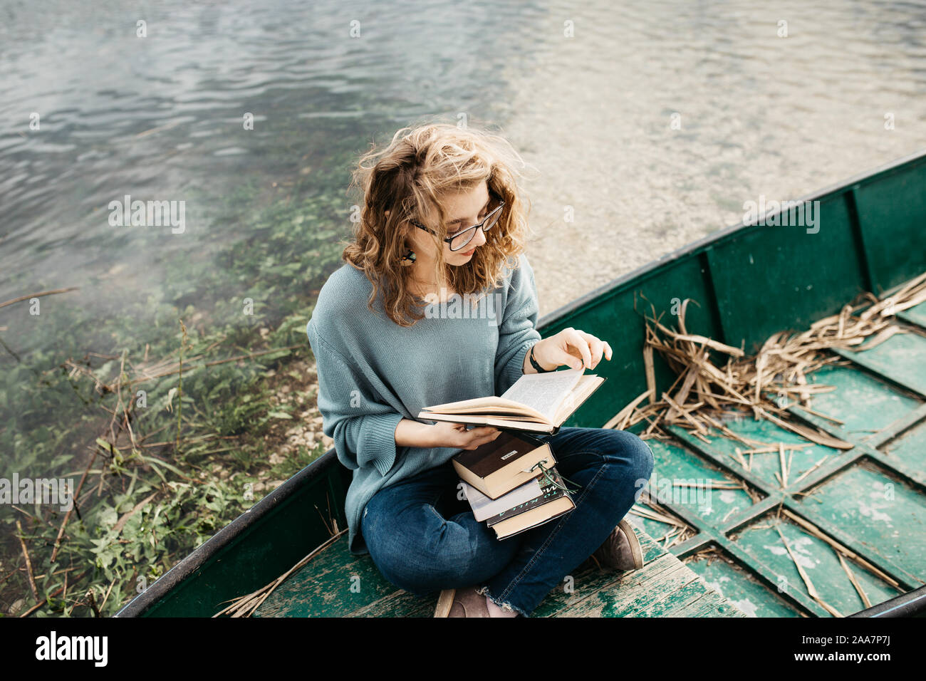 Porträt der jungen schönen Frau, die auf einem Boot sitzt und ein Buch liest. Sie ist Bücherwurm und sie wählt zwischen wenigen Büchern. Stockfoto