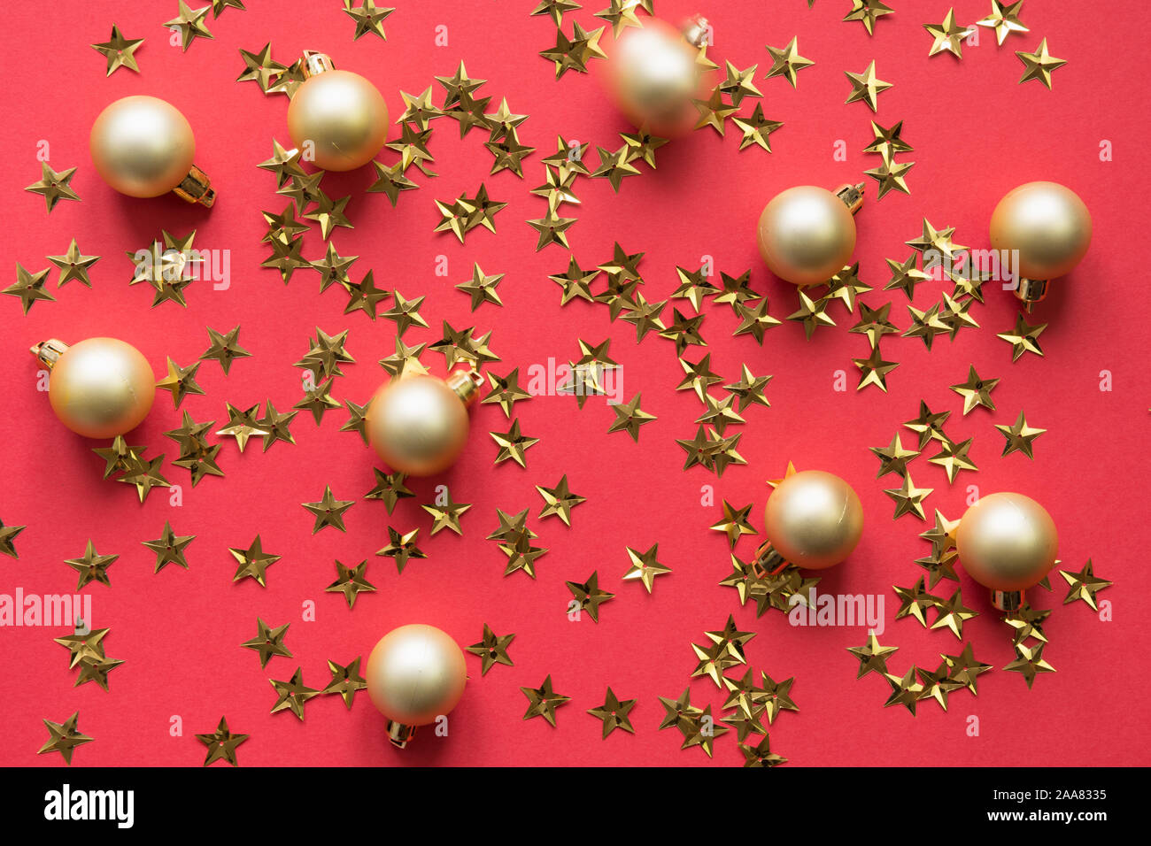 Goldene Kugeln und Sterne glitter Konfetti auf rotem Hintergrund. Party Urlaub Kulisse. Ansicht von oben, flach Stil. Stockfoto