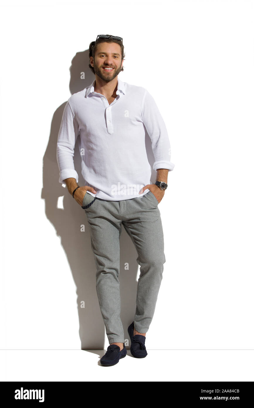 Entspannt gut aussehender Mann in Mokassins, graue Hose, weißes Hemd steht  gegen sonnigen Wand mit Händen in den Taschen und lächelnd. Volle Länge  studio Stockfotografie - Alamy