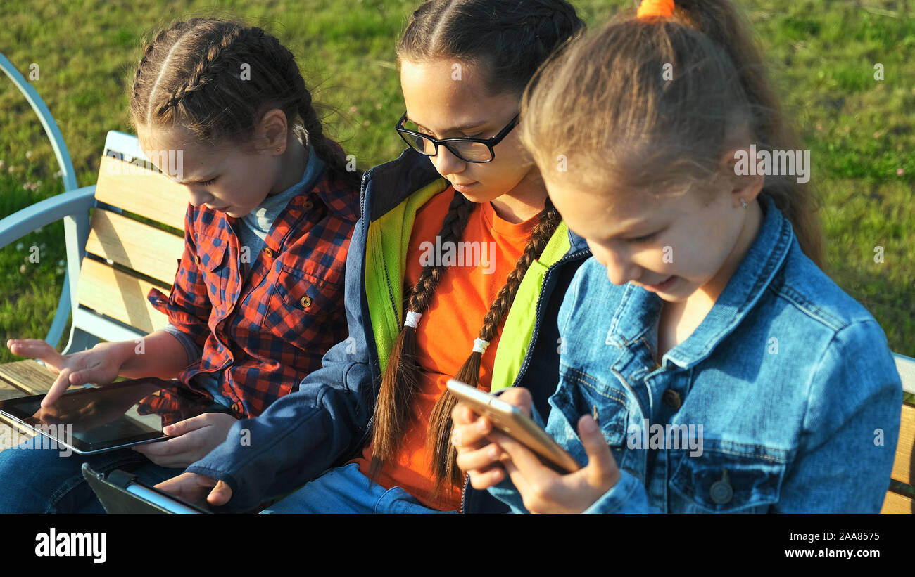 Drei Kinder Mädchen sitzen auf einer Bank und Blick auf Tablet-PCS und Smartphones. Stockfoto