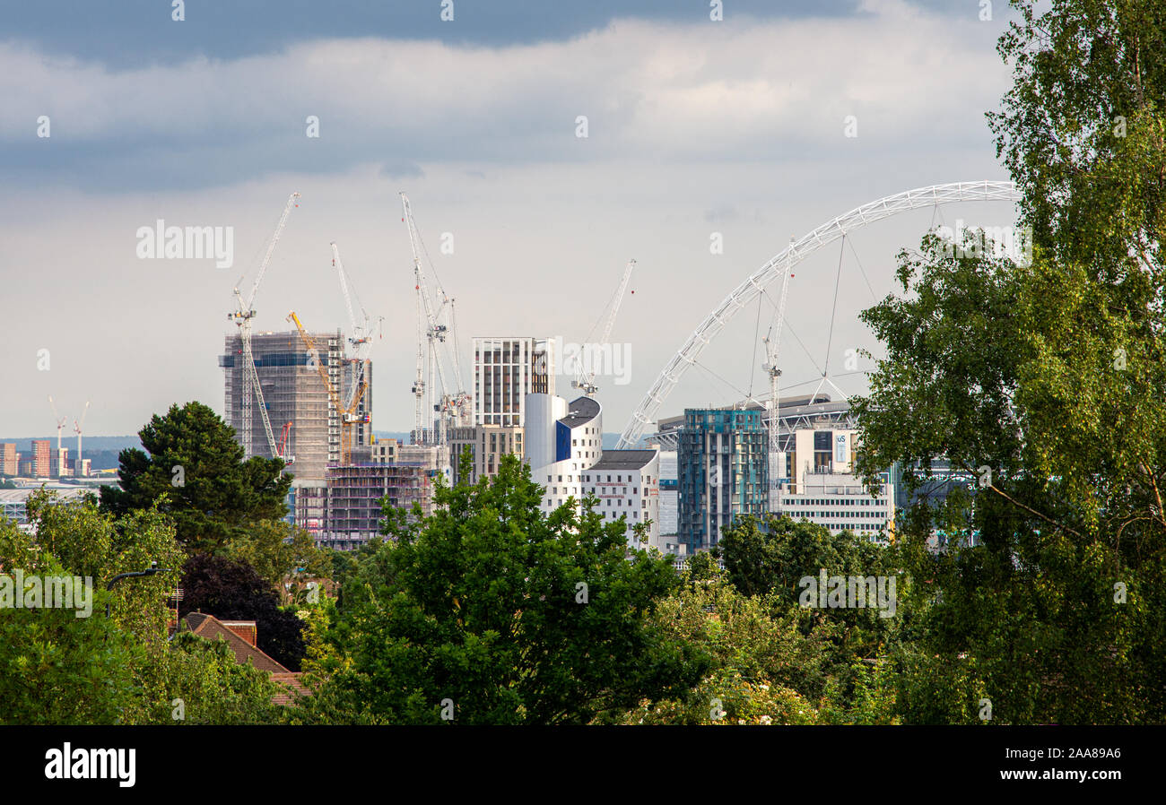 London, England, UK - Juli 7, 2019: Das Wembley Stadion Arch und Hochhaus neue Gebäude scheinen, über die Bäume des Barn Hill Park in London. Stockfoto