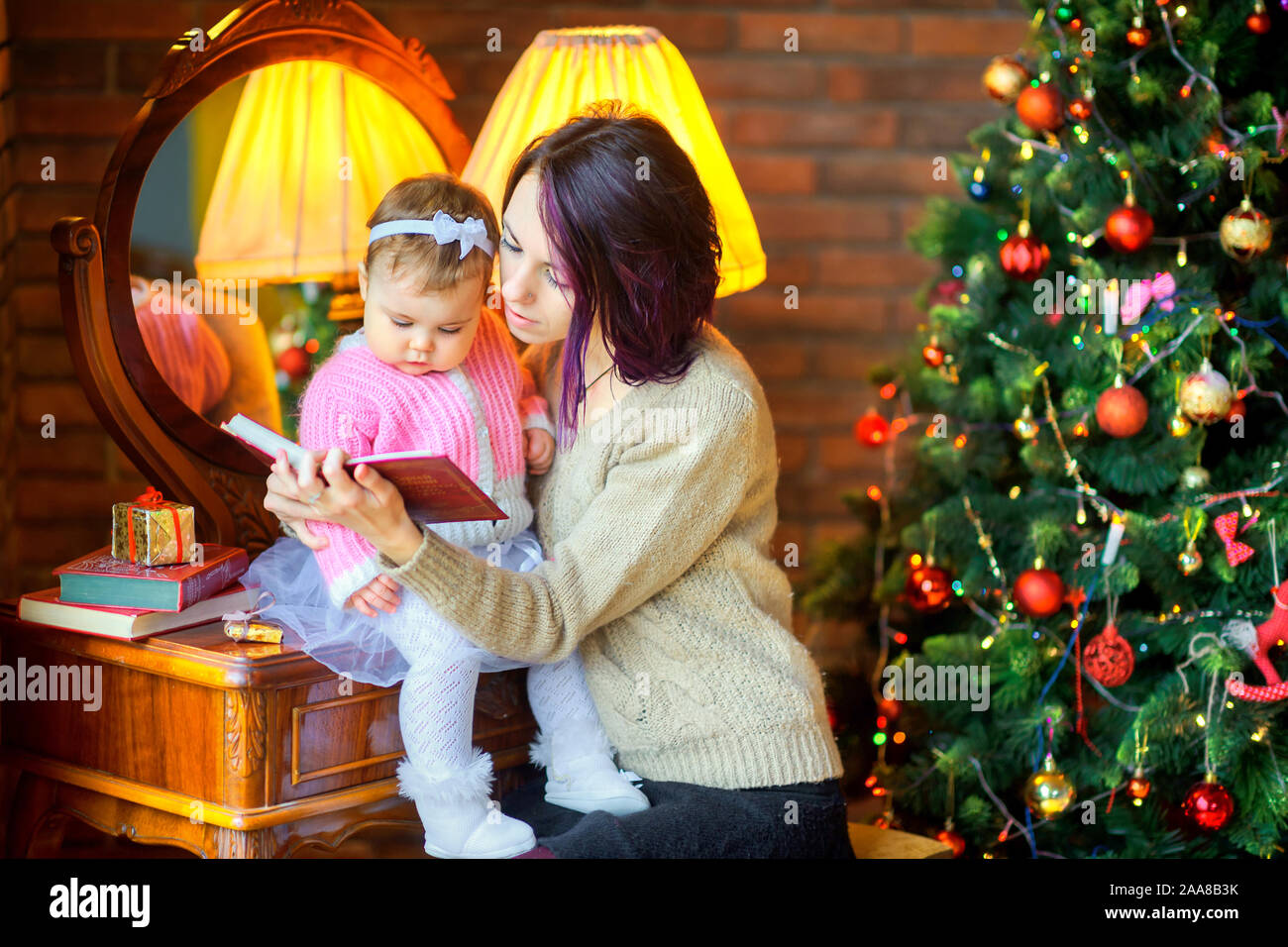 Mama liest eine kleine Tochter Weihnachten Geschichten neben dem Holiday tree. Warten auf den Urlaub. Stockfoto