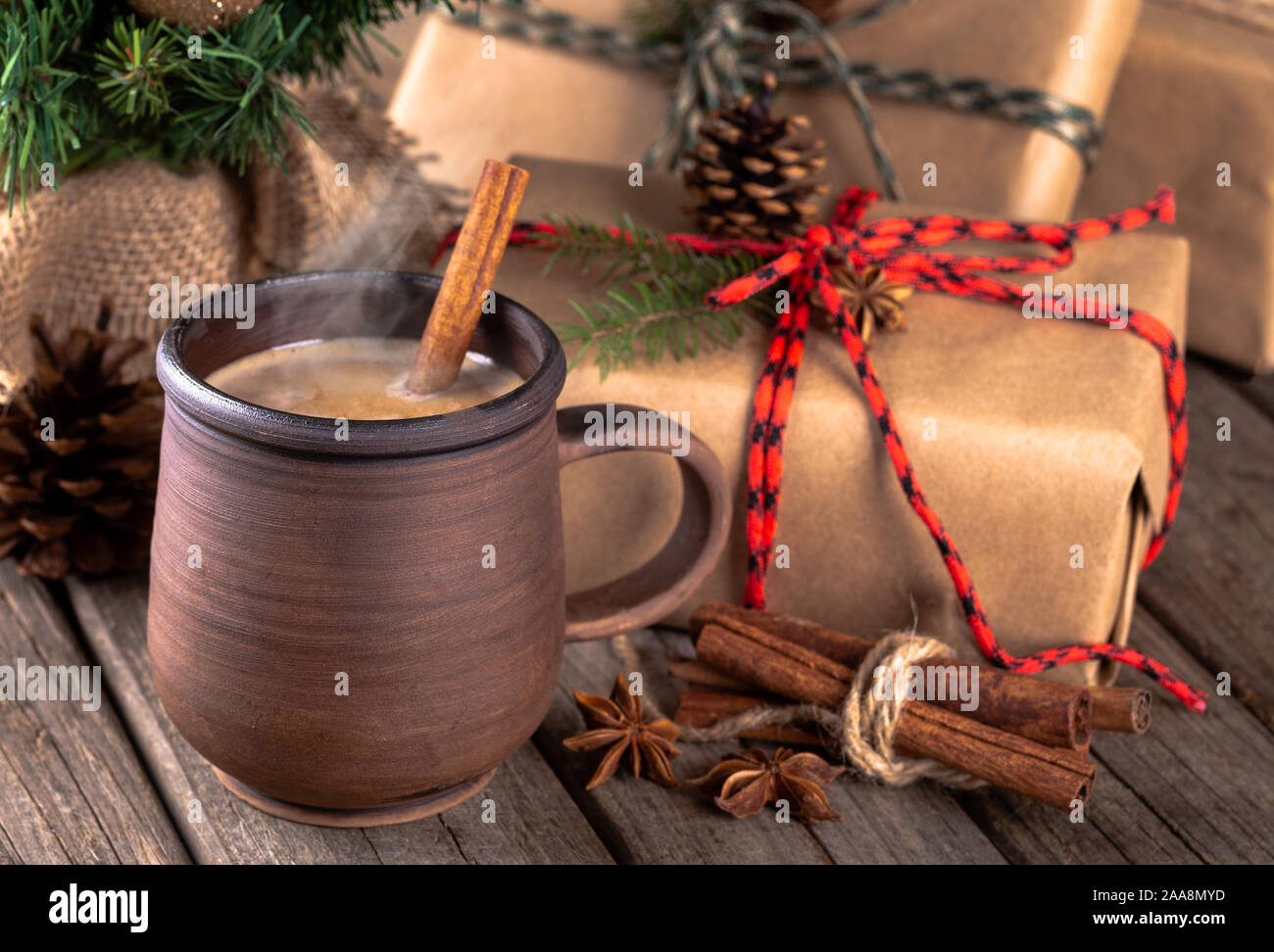 Nahaufnahme von einem heißen Getränk in eine braune Tasse mit Zimtstangen und Weihnachtsgeschenke im Hintergrund auf einem rustikalen hölzernen Oberfläche Stockfoto