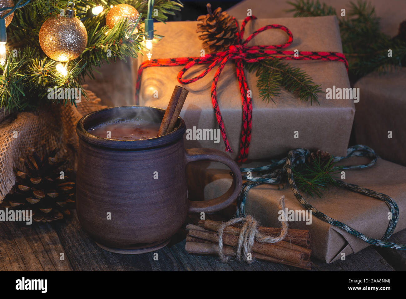 Nahaufnahme der heiße Schokolade in eine braune Tasse mit Weihnachten Geschenke und Baum im Hintergrund auf einem rustikalen hölzernen Oberfläche Stockfoto
