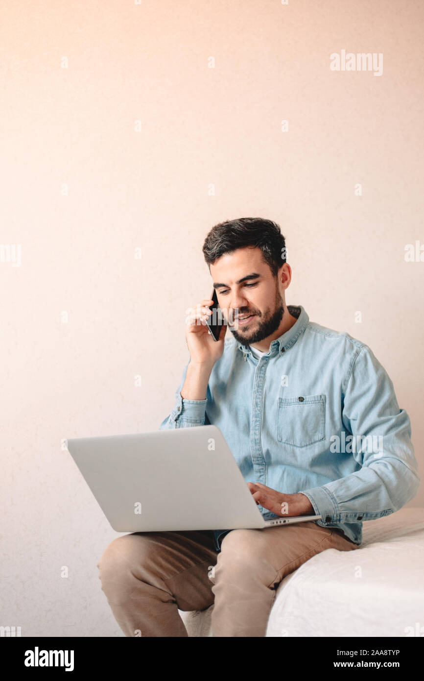 Mann auf Smart Handy mit Laptop zu Hause sitzen Stockfoto