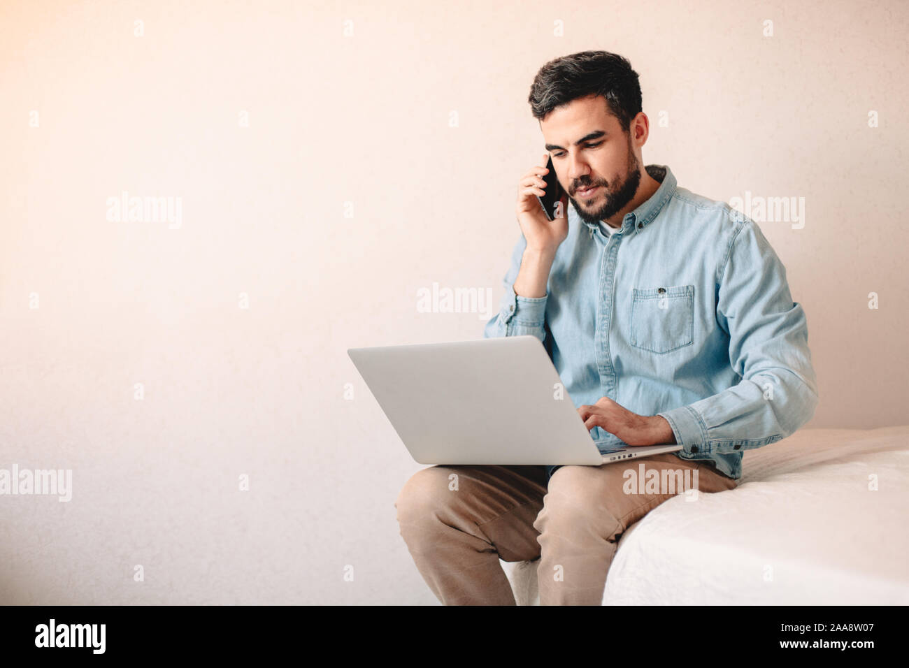 Mann auf Smart Phone, während mit Laptop Computer zu Hause. Stockfoto