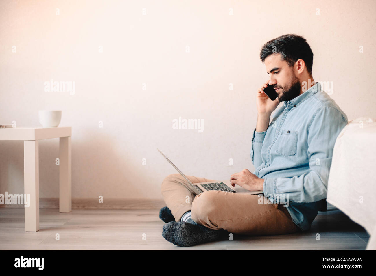Mann auf smart phone mit Laptop sitzen auf dem Boden gegen die Wand Stockfoto