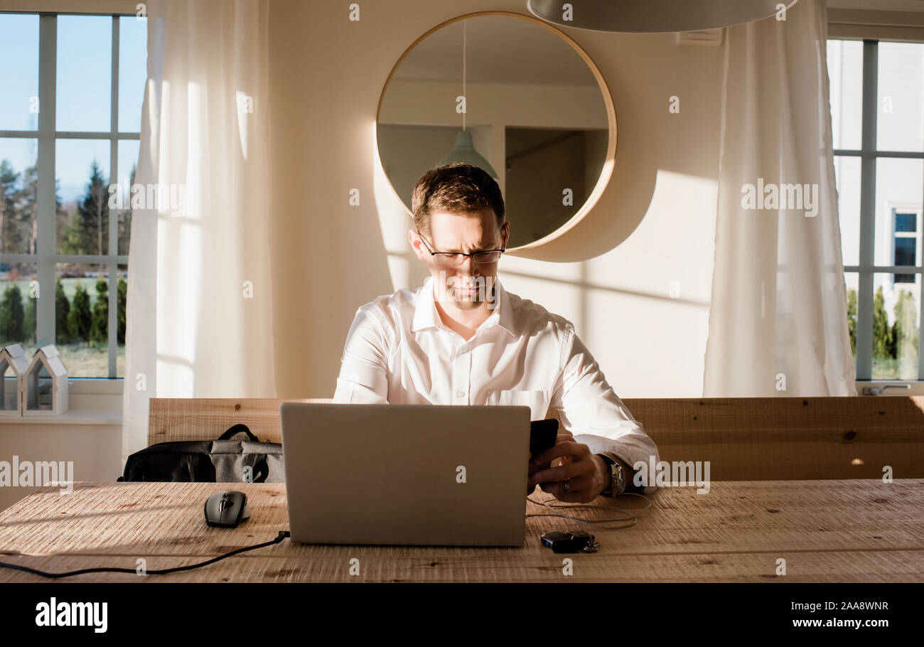 Mann bei der Arbeit von zu Hause aus auf sein Handy und Laptop konzentrieren. Stockfoto