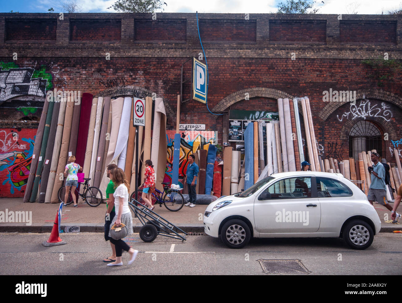 Fußgänger vorbei Teppiche für Verkauf an Sclater Straße Fleat Markt im East End von London. Stockfoto