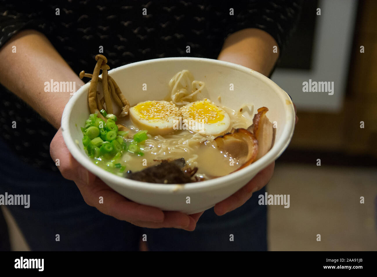 Frau Hände halten eine Schüssel mit traditionellen Japanischen Schweinefleisch Ramen Suppe, mit enoki Pilze, mittlere gekochte Eier, Schalotten, Algen und Schweinefleisch Stockfoto