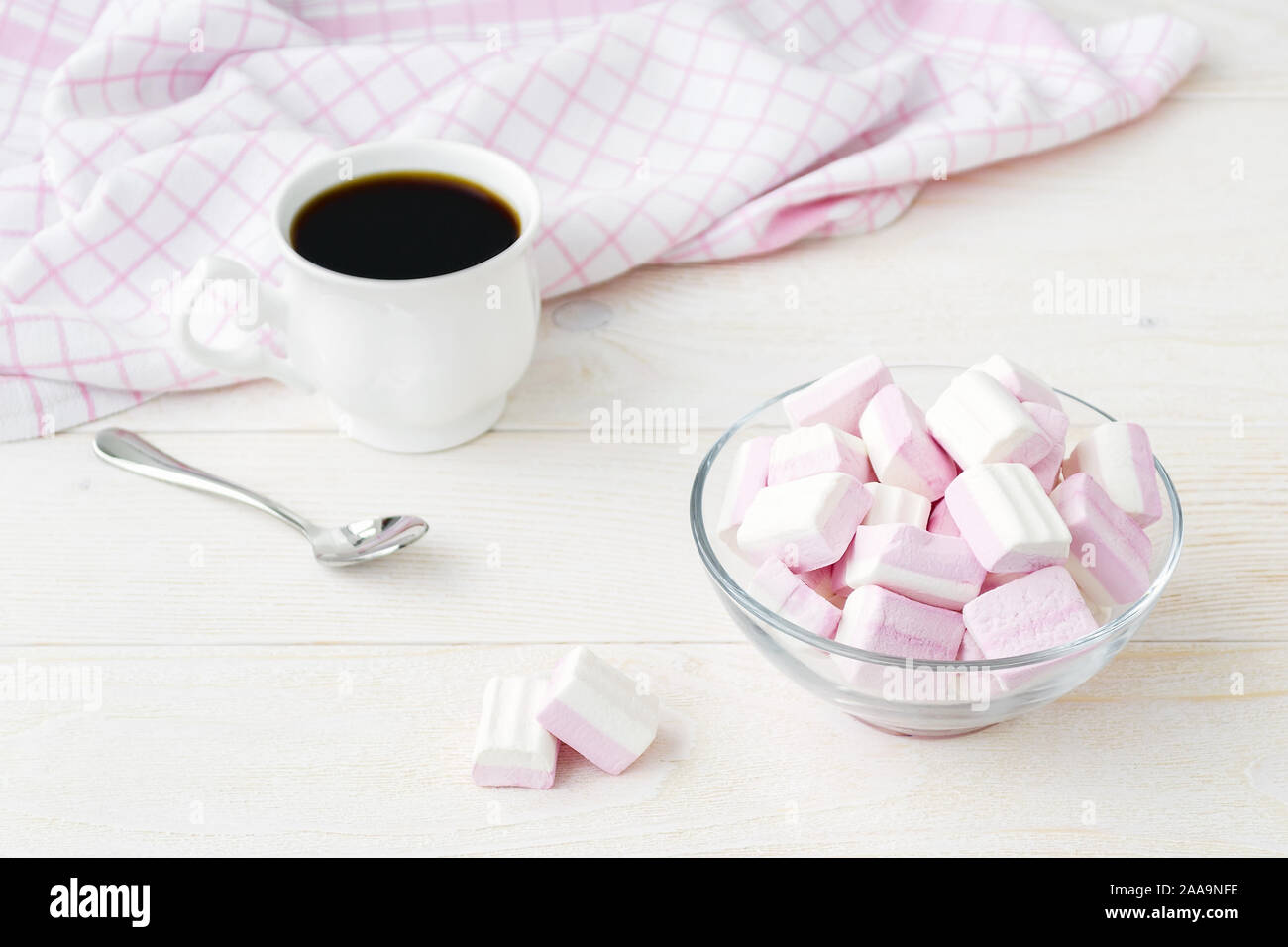 Weiß rosa Flauschige Marshmallows in eine Glasschüssel und eine Tasse Kaffee auf hellem Holztisch. Süß und lecker Essen im Winter. Köstliche weiche Süßigkeiten. Stockfoto