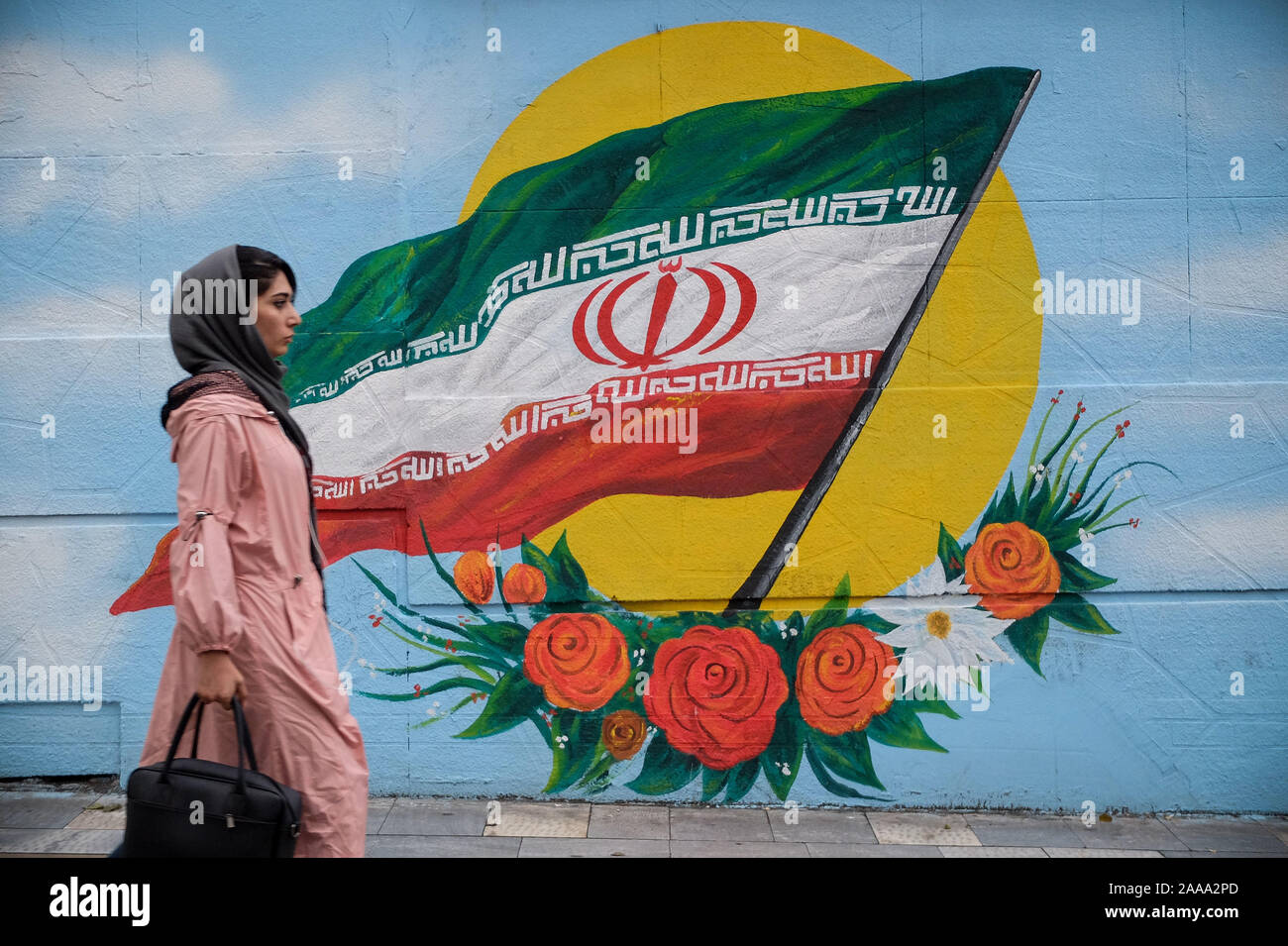 Teheran, Iran. Nov, 2019 20. Eine iranische Frau geht neben einem Wandgemälde des iranischen Nationalflagge in Teheran, Iran. Iran am 15. November die gestiegenen Kraftstoffpreise um mindestens 50 Prozent fordert Proteste in verschiedenen Städten. Präsident Hassan Rohani sagte, die Menschen des Landes besiegt hatte eine "feindliche Verschwörung'' hinter einer Welle von gewalttätigen Demonstrationen. Demonstrationen ausgebrochen in Sanktionen - schlagen Sie dem Iran in der vergangenen Woche nach einer Ankündigung der Benzinpreise um bis zu 200 Prozent angehoben werden, mit Autofahrer blockieren wichtige Straßen in Teheran vor den Unruhen rasch auf mindestens 40 städtische Ausbreitung Stockfoto