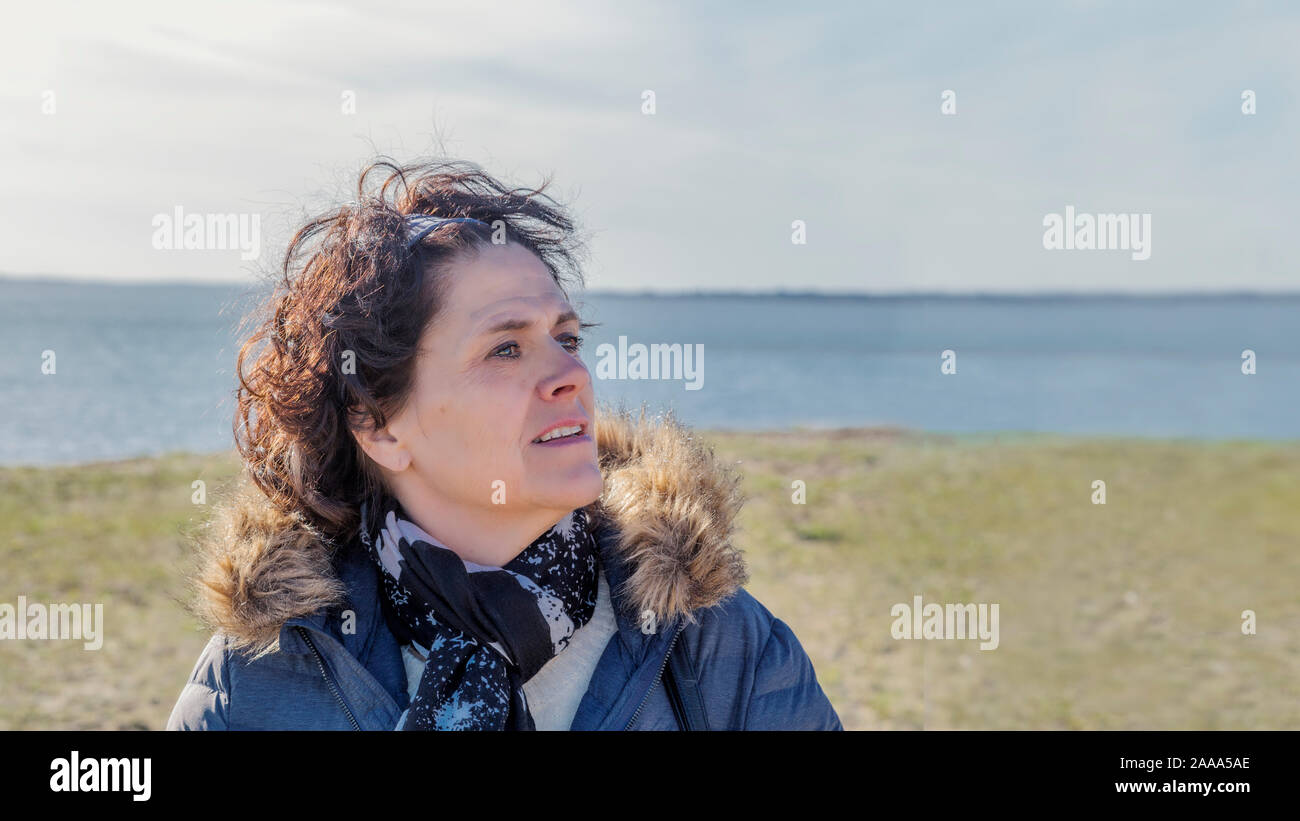 Eine Frau mittleren Alters an der Küste in casual Winter Kleidung sieht die Seite voller Optimismus, Hoffnung und Glück. Kopieren Sie Platz an der Seite. Stockfoto