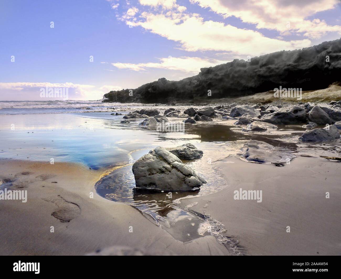 Detail einer Lava Sandstrand mit Ablassen von Wasser am Atlantik auf Teneriffa. Im Vordergrund eine große Lava Stein mit Fokus auf den Stein. Blau Stockfoto