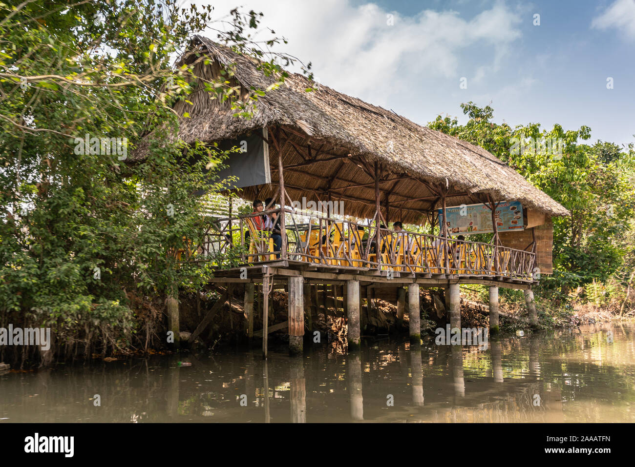 Cai, Mekong Delta, Vietnam - März 13, 2019: Entlang der Kinh 28 Kanal. Kaffee Errichtet auf Stelzen auf braunem Wasser und mit Strohdach und gelb Chai Stockfoto