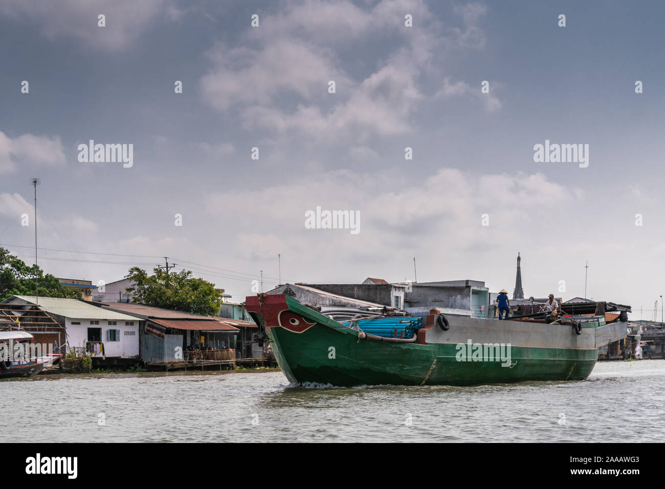 Cai, Mekong Delta, Vietnam - März 13, 2019: Entlang der Kinh 28 Kanal. Grüne Lastkahn mit blauen Leitungen Segel unter blauem cloudscape geladen. Schlechte Wohnverhältnisse auf s Stockfoto