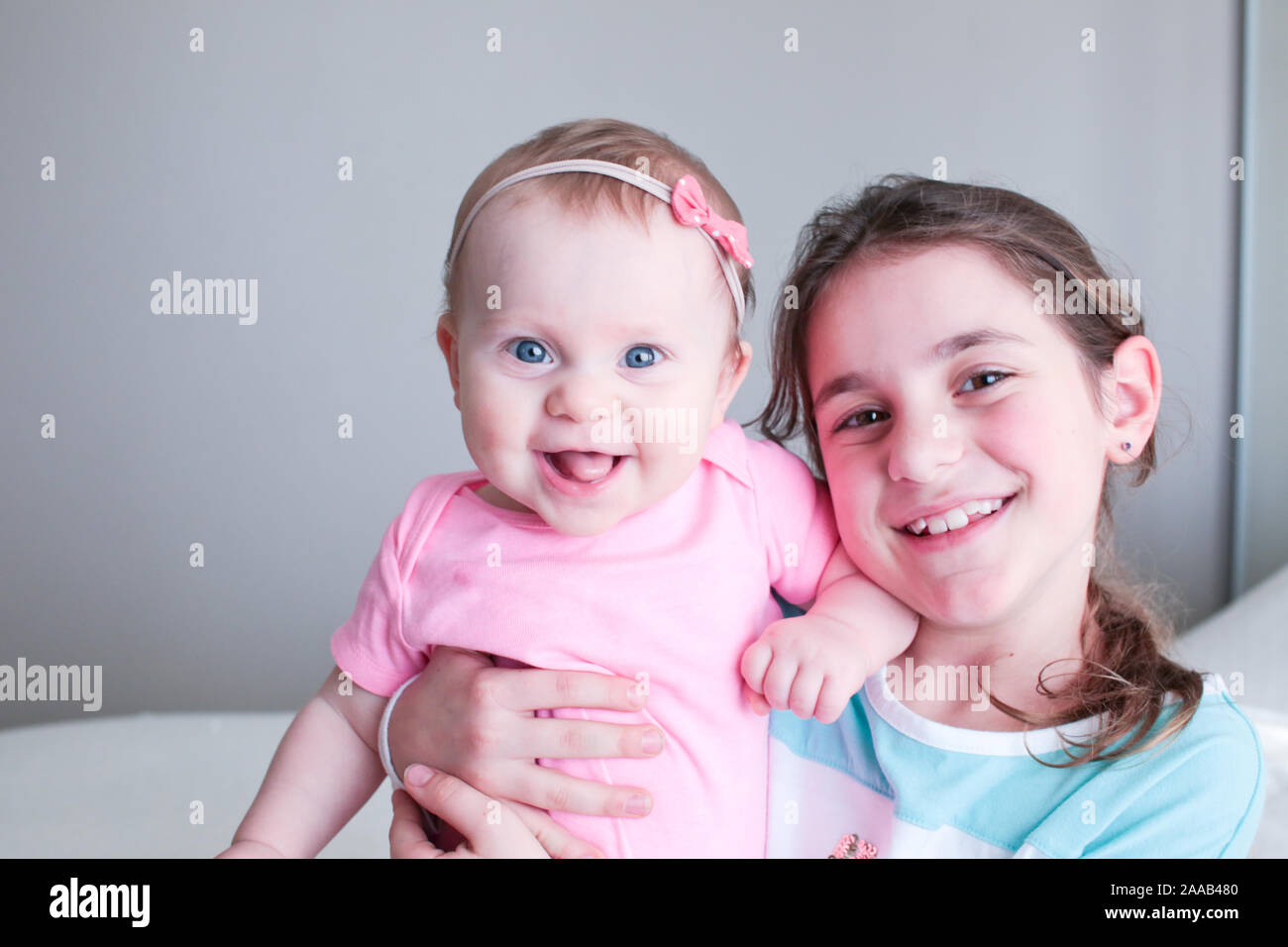 Nahaufnahme, Porträt von zwei Schwestern, süßen 8 Monate alten Baby Girl mit großen blauen Augen und 8 Jahre alte Schule Alter Mädchen mit braunen Augen, Happy Baby Girl Stockfoto