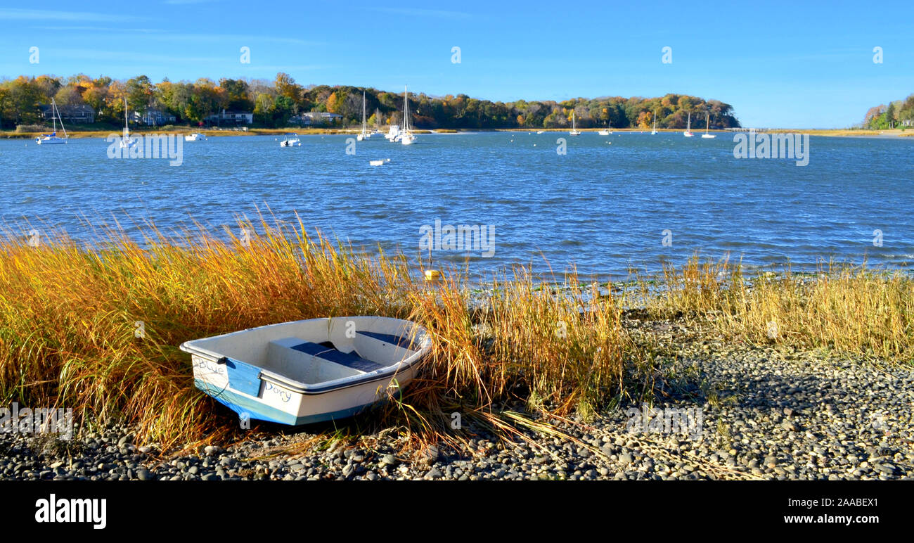 Herbsttag mit Ruderboot am Hafen Ufer mit orange braun Gras und bewaldeten entfernten Ufer im Herbst Laub. Stockfoto
