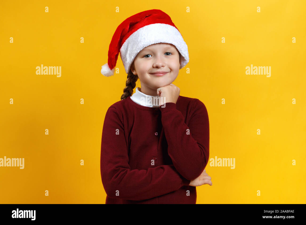Weihnachten und Neujahr Konzept. Bezaubernde Kind in einem Santa Hut auf einem gelben Hintergrund niedlich. Kleines Mädchen lächelt und Träume. Stockfoto