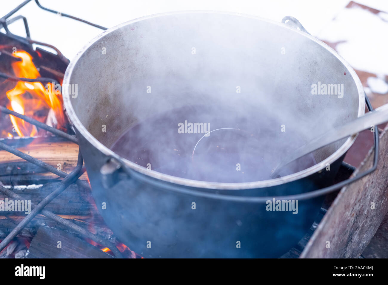 Bei einem Feuer in einem Topf Vorbereitung Glühwein. Hot rot Wein am offenen Feuer im Winter Stockfoto