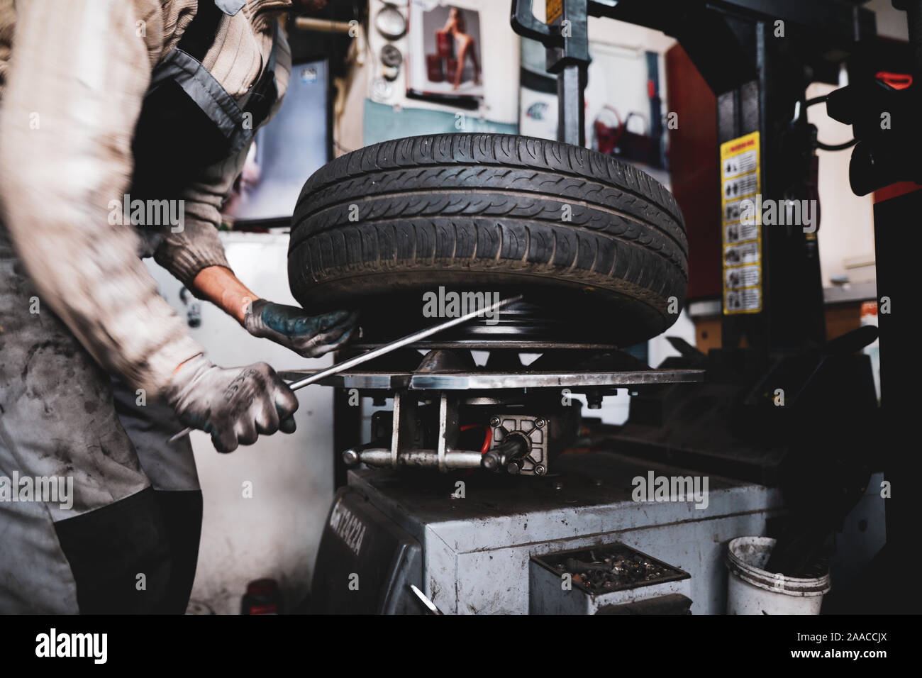 Flache Tiefenschärfe (selektive Fokus) Bild mit einem Mechaniker Ändern der regelmäßigen Sommer Reifen eines Autos mit Winterreifen in einem dreckigen Auto Service. Stockfoto
