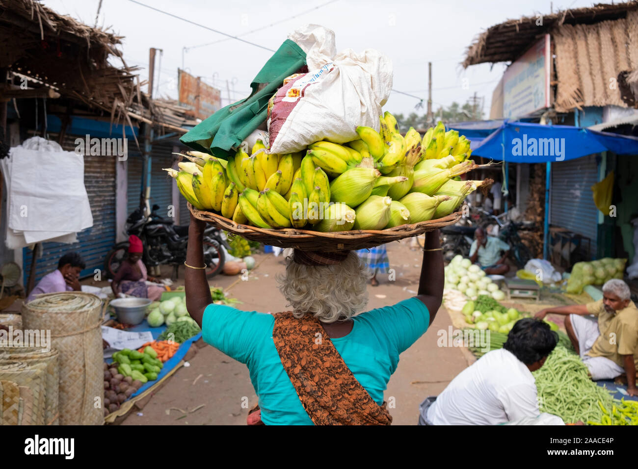 Alte Frau, die ein Korb mit Obst für den Verkauf auf dem Kopf im freien Markt in Tiruchirappalli, Tamil Nadu, Indien Stockfoto