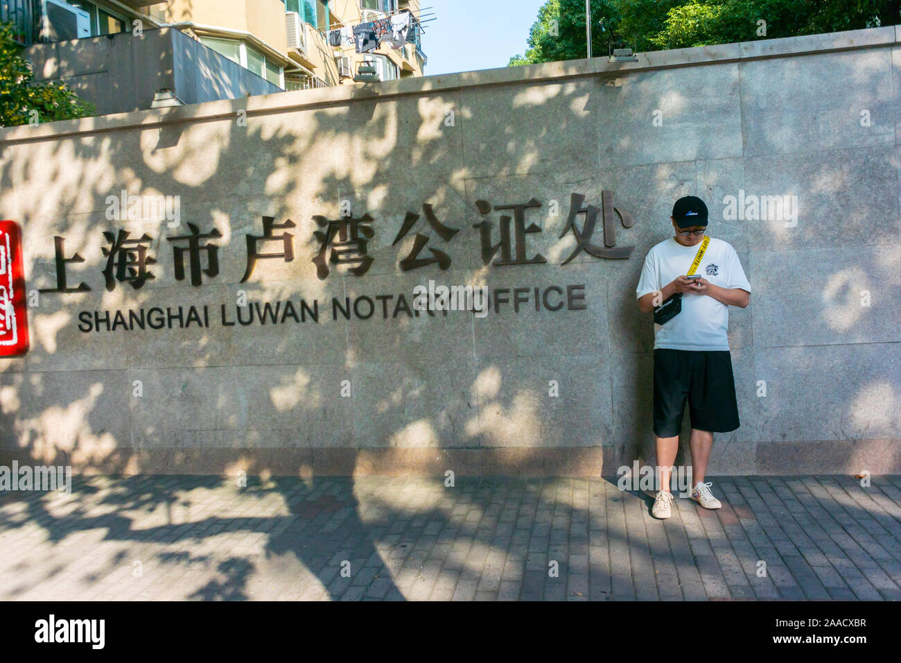 Shanghai, China, Mann steht draußen, Blick auf Smartphone, Regierungsgebäude, Notariatsbüros, chinesische Stadt Straße öffentliche andere Sprachschild china Stockfoto