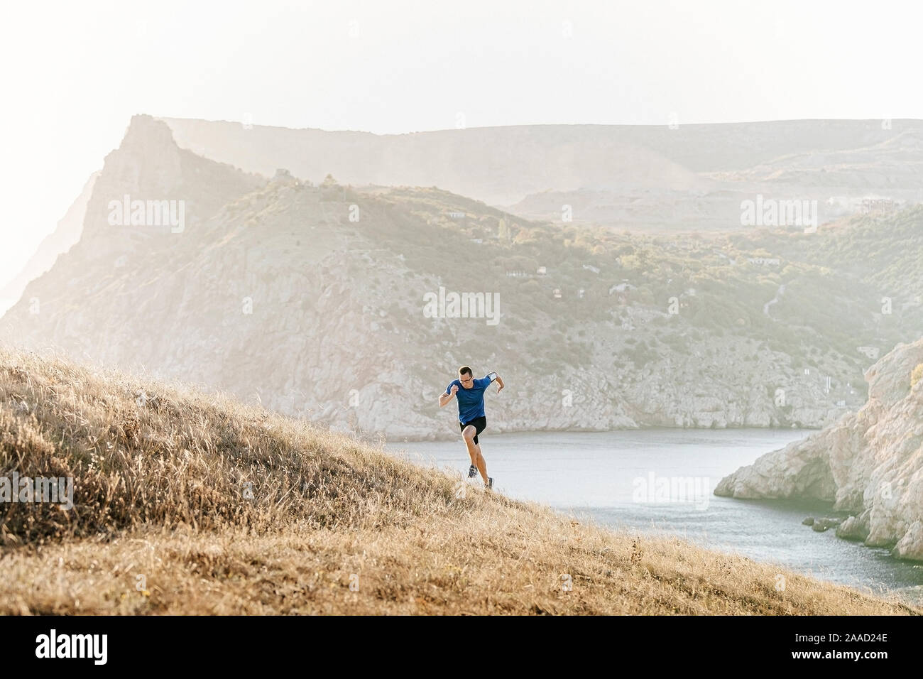 Männliche Läufer mit Brille bergauf läuft im Sonnenuntergang, Armband mit Handy Stockfoto
