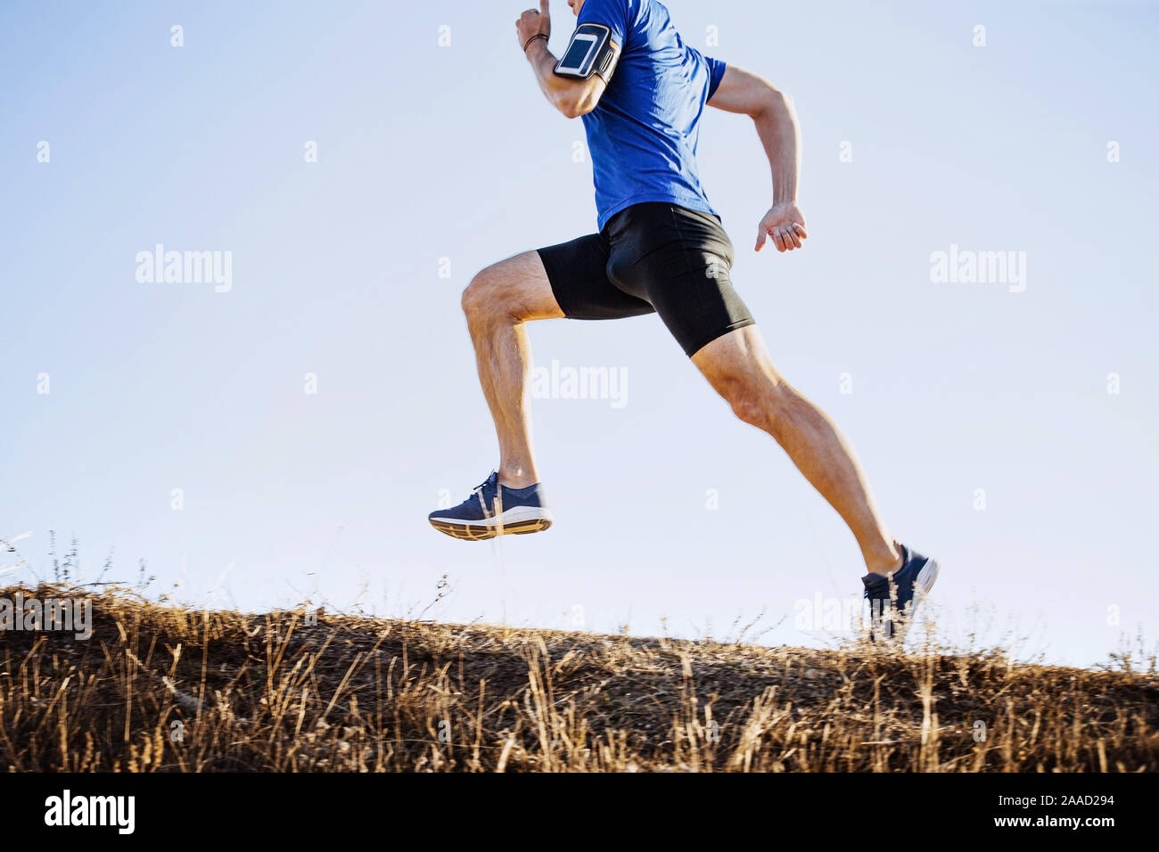 Männliche Läufer laufen bergauf, Armband mit Handy Stockfoto
