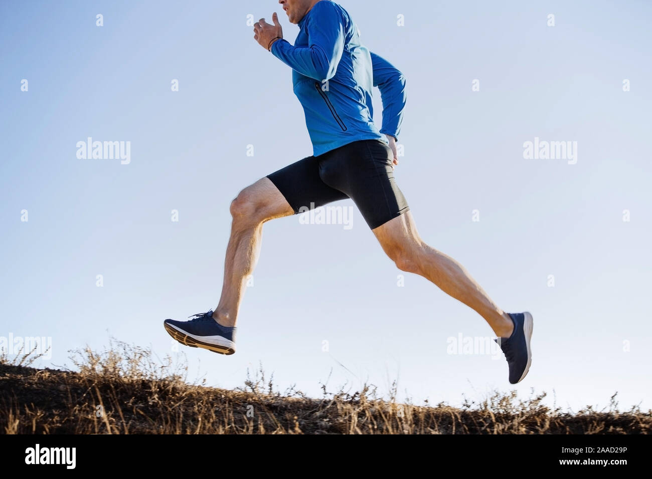 Männliche Läufer bergauf in der blauen Jacke und schwarzen engen Hose läuft Stockfoto