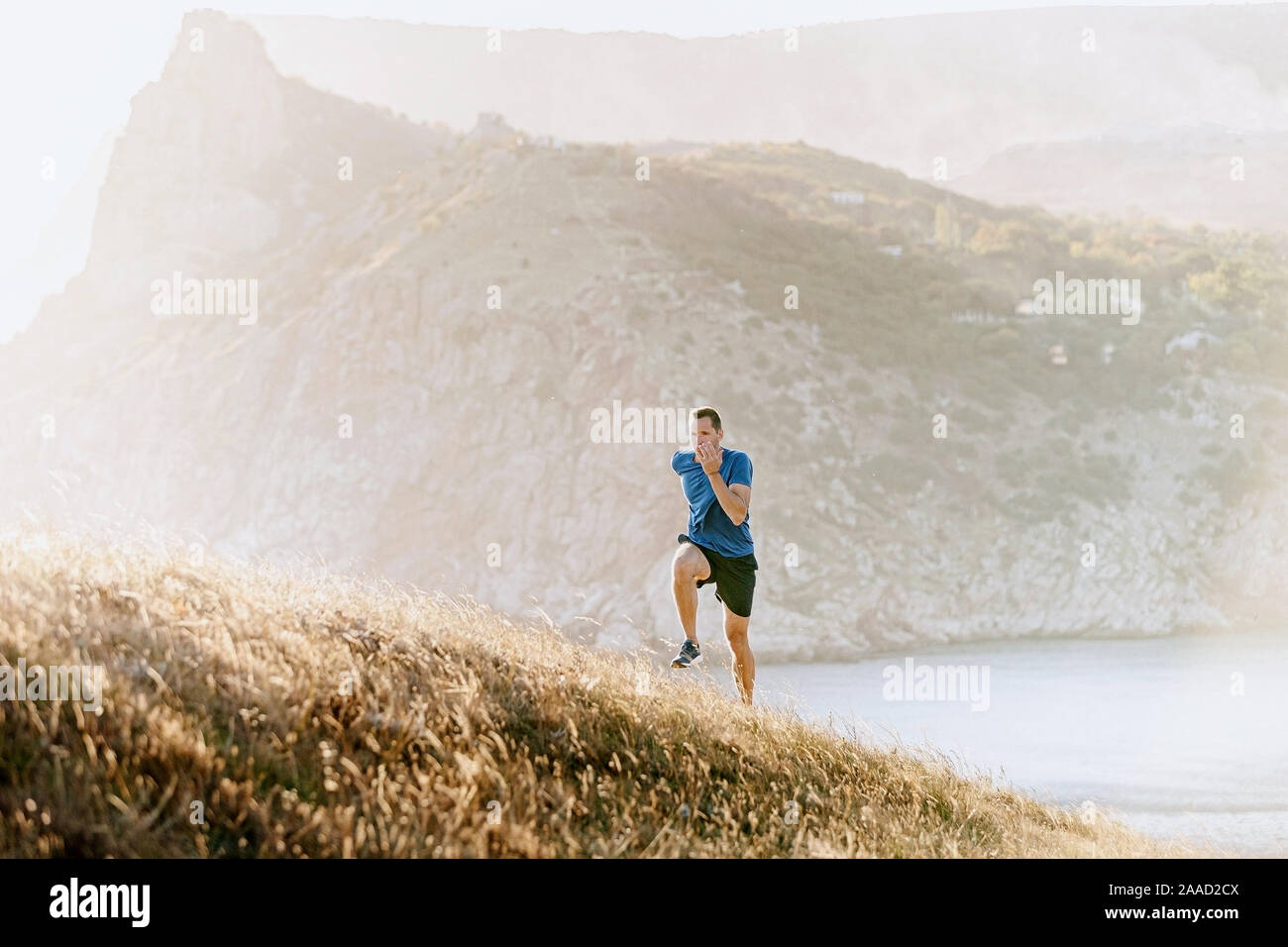 Männliche Läufer laufen bergauf im Sonnenuntergang Meer Bay Stockfoto