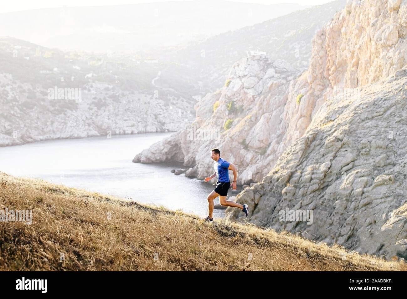 Sportliche Mann bergauf laufen im Hintergrund die Berge und das Meer Stockfoto