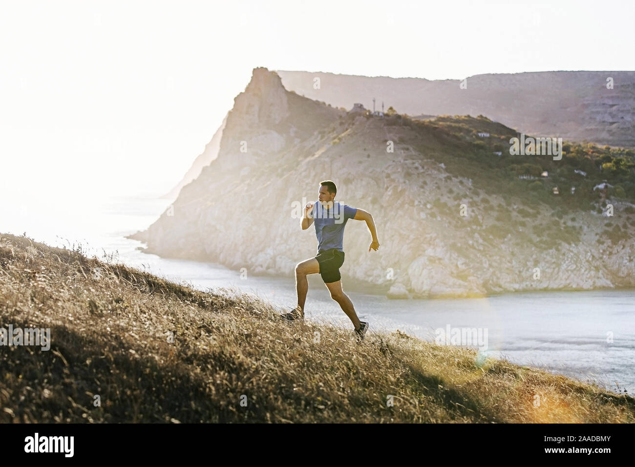 Sportlicher Mann mit Mountain Trail in bergauf bei Sonnenuntergang und Sonnenlicht Stockfoto