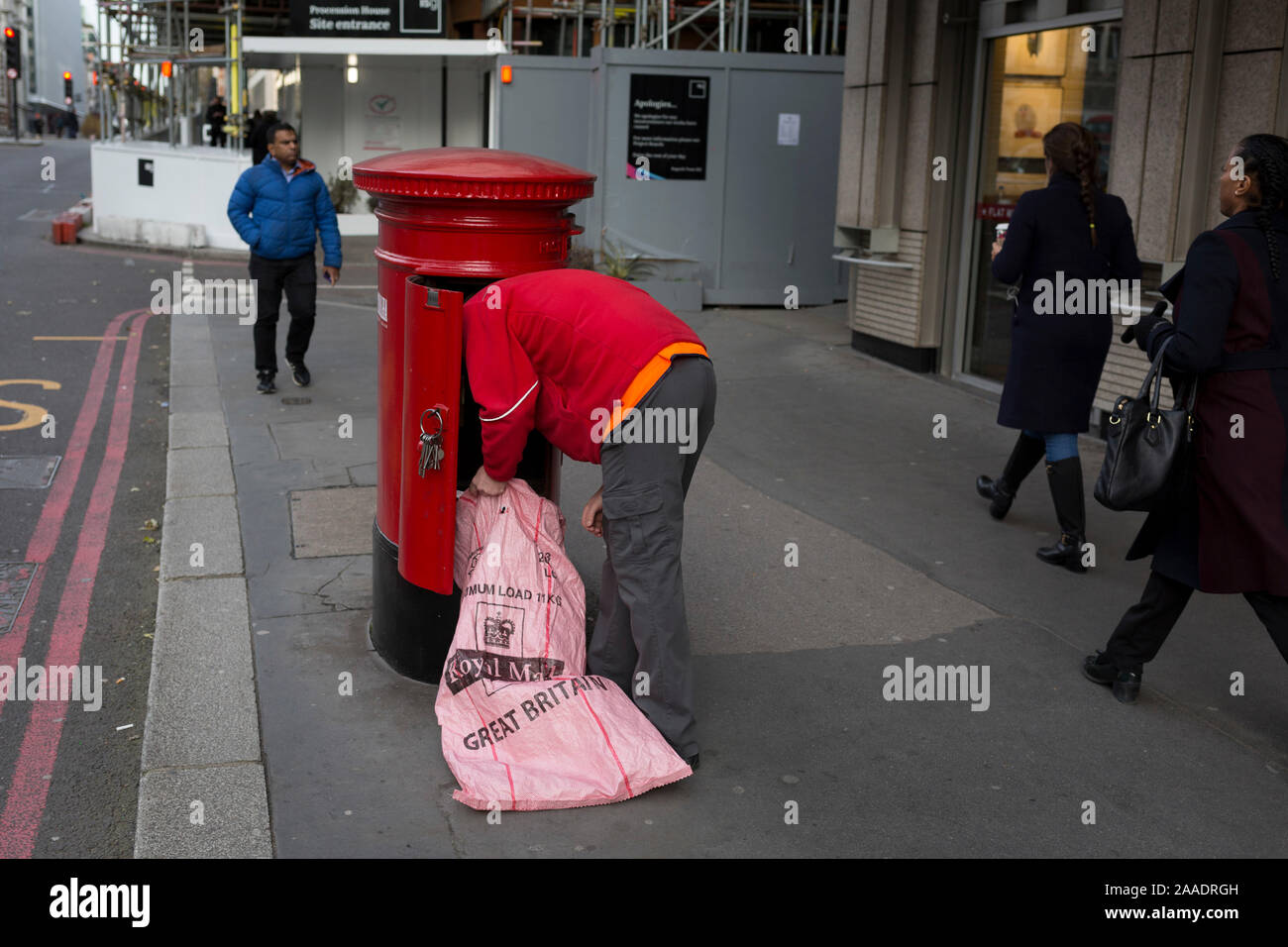 Ein Royal Mail Arbeiter und lehnt sich in ein Postfach ein Stapel von Briefen und Paketen zu leeren, am 20. November 2019, in der City von London, England. Stockfoto