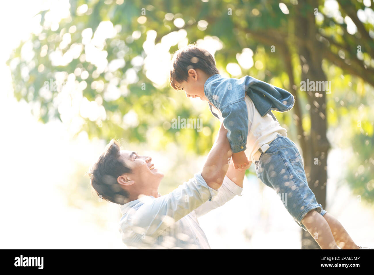 Süße kleine asiatische Junge von Vater draußen im Park angehoben Stockfoto