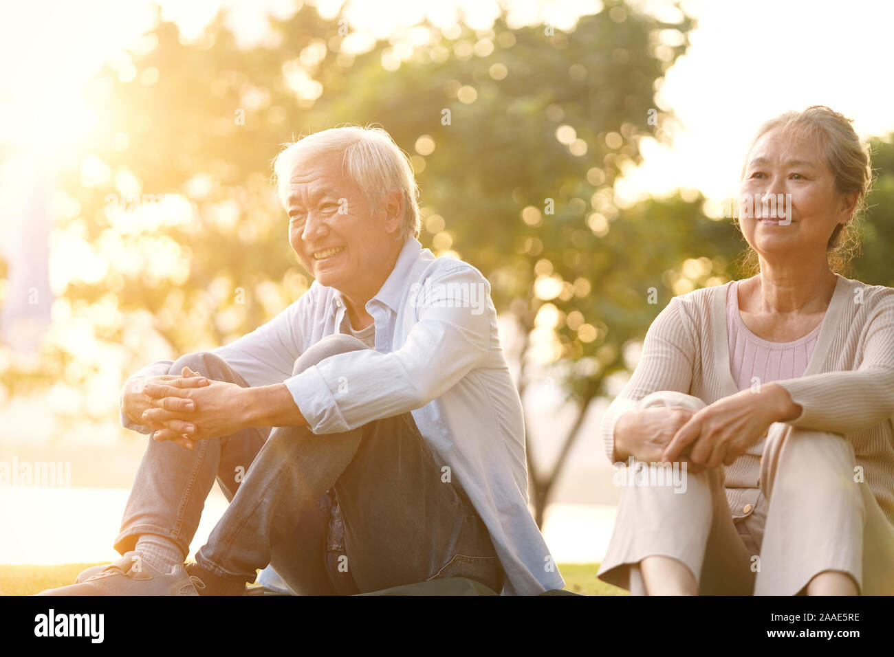 Asiatische senior Paar sitzt auf Gras Sonnenuntergang draußen im Park Stockfoto