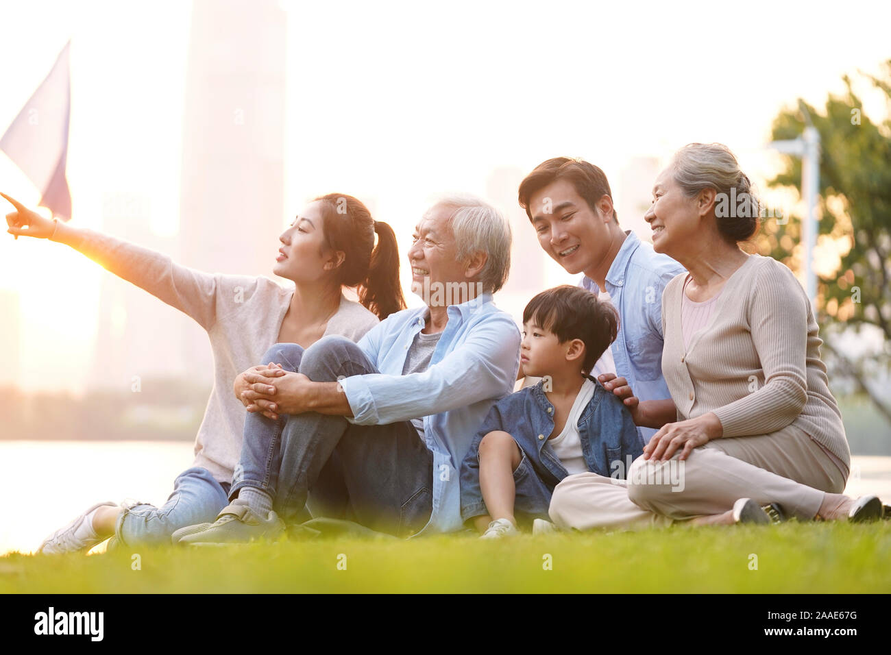 Drei generation gerne asiatische Familie sitzt auf dem Rasen eine gute Zeit in der Dämmerung im Freien in Park Stockfoto