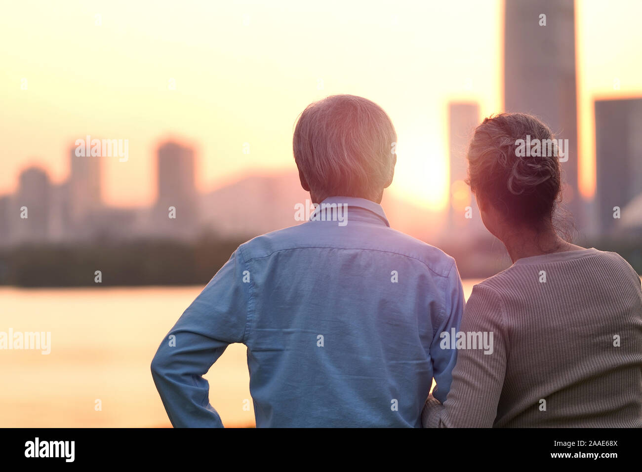 Ansicht der Rückseite des Älteren asiatischen Paar suchen bei Sonnenuntergang und die Skyline der Stadt vom Fluss Stockfoto