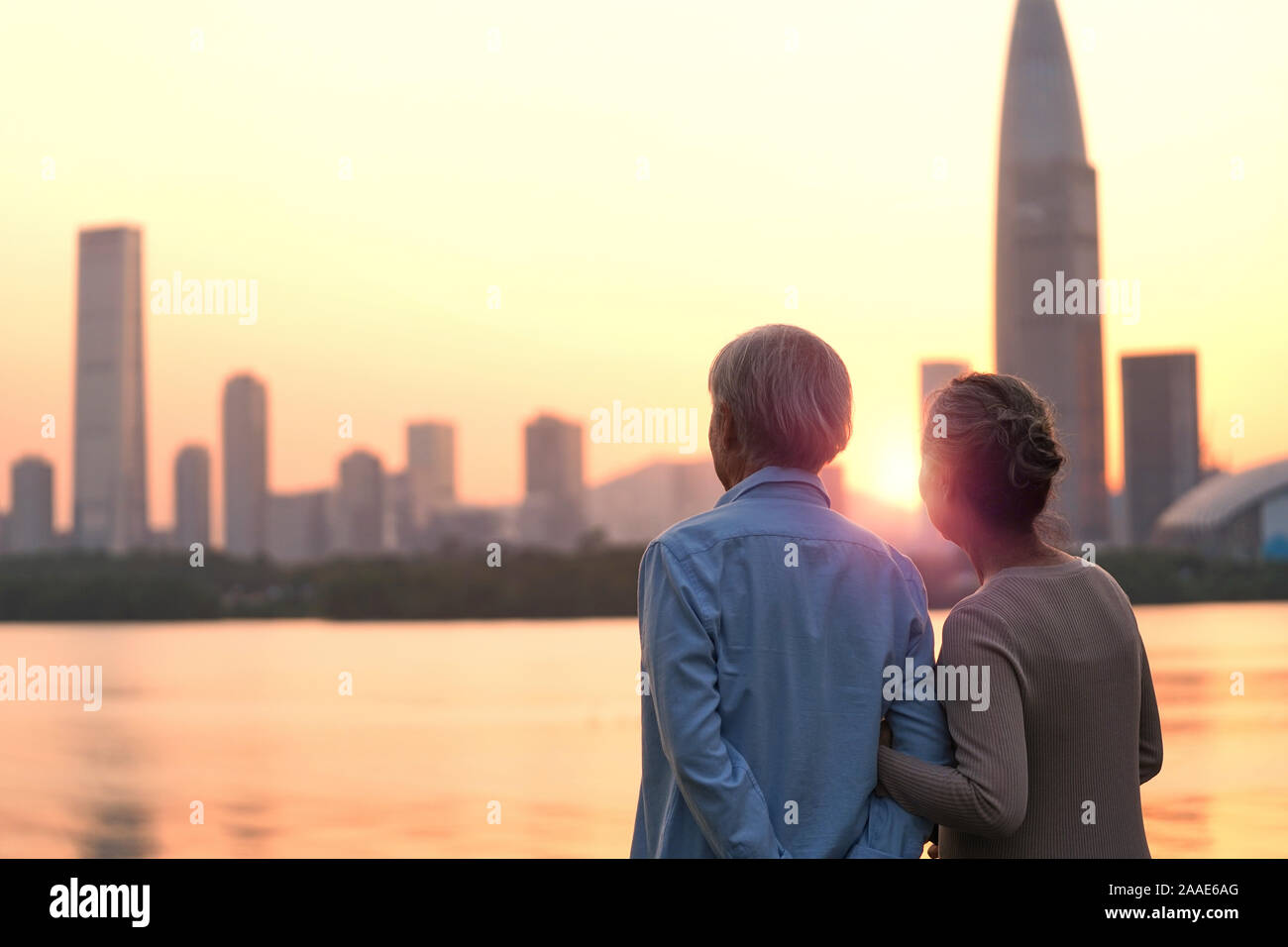 Ansicht der Rückseite des Älteren asiatischen Paar suchen bei Sonnenuntergang und die Skyline der Stadt vom Fluss Stockfoto