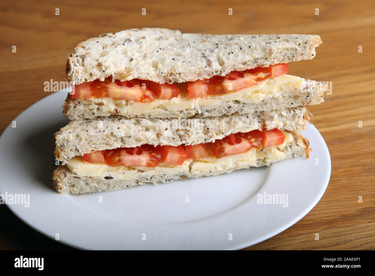 Ein Käse und Tomaten Sandwich serviert mit mehrkornbrot in der Hälfte auf weiße Platte auf hölzernen Tisch Stockfoto