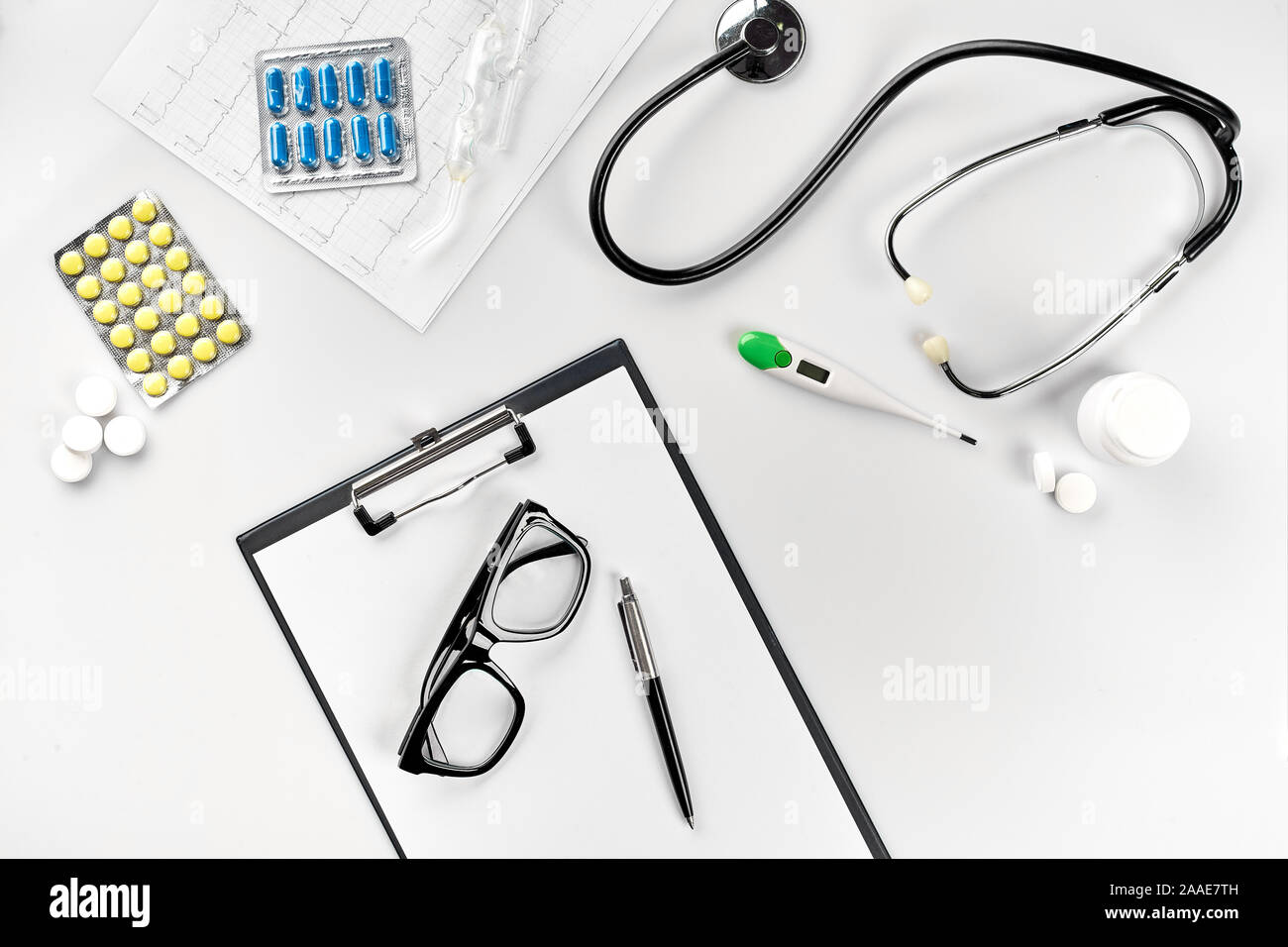 Geschäft für Krankenhaus: Pillen, Stethoskop, medizinische Geräte, Notizbuch mit Stift und Gläser auf weißem Hintergrund. Der moderne Doktor auf dem Tisch Stockfoto
