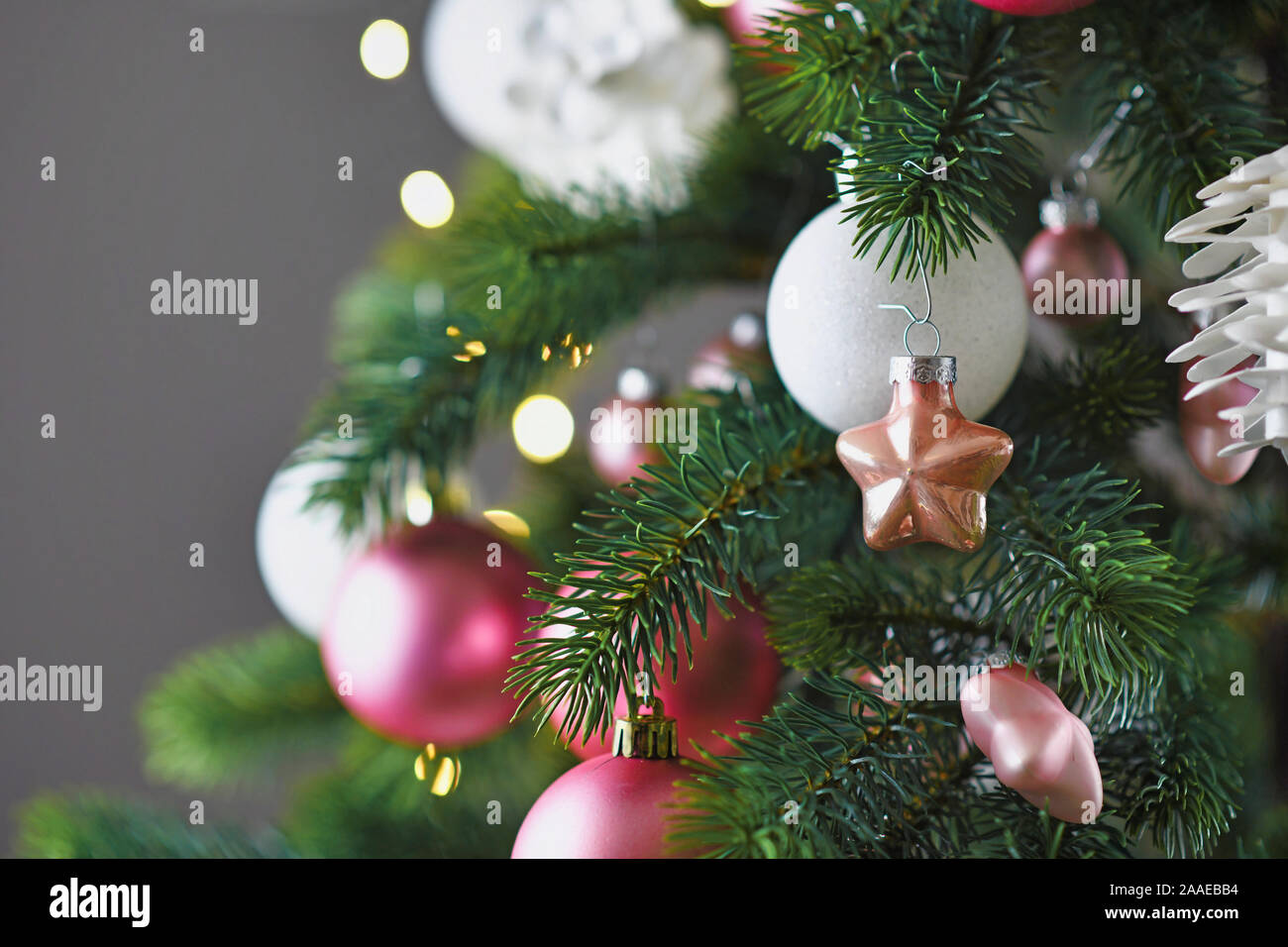 Close up pf geschmückten Weihnachtsbaum mit weißen und rosa Saison baumschmuck wie Kugeln und Sterne auf grauem Hintergrund Stockfoto