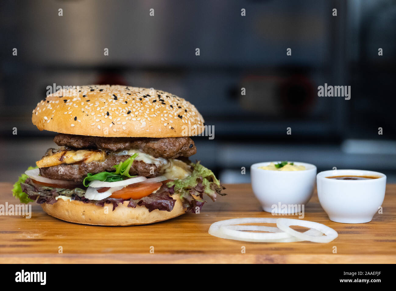 Eine große Frische bunte Burger mit Fleisch, Eier, Salat, Zwiebeln und Dips auf einer hölzernen Fach-up schließen Stockfoto