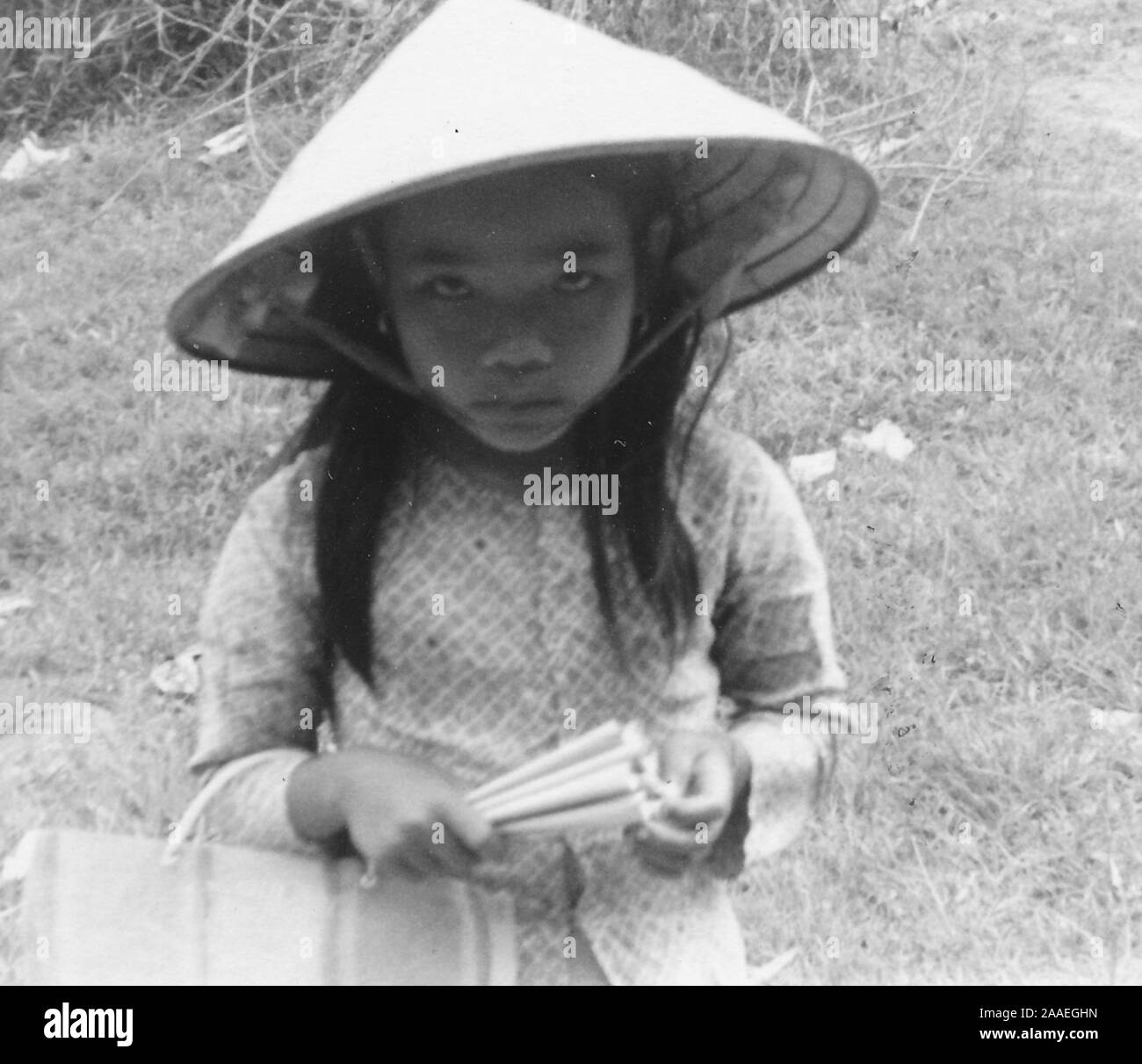 High-Angle Shot eines kleinen Mädchens, das von der Taille bis, das Tragen einer Konischen nicht La hat und mit einem Ventilator und Handtasche, in Richtung Kamera schaut mit einem ernsten Ausdruck auf ihrem Gesicht, Vietnam, 1966. () Stockfoto