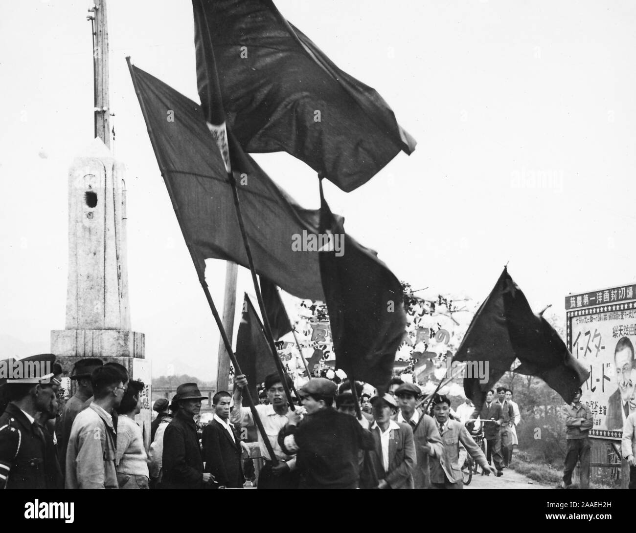 Eine flag-waving Masse der Demonstranten marschiert in Richtung der Kamera an einem bewölkten Tag, mit Passanten, einschließlich Polizisten, ihre Fortschritte beobachten von beiden Seiten der Straße, in der Präfektur Fukuoka, Japan, 1950. () Stockfoto